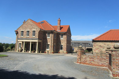 Immagine della facciata di una casa grande rossa country a due piani con rivestimento in mattoni e tetto a padiglione
