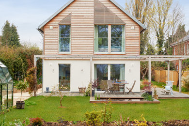 This is an example of a small and beige farmhouse two floor house exterior in Hampshire with wood cladding and a pitched roof.