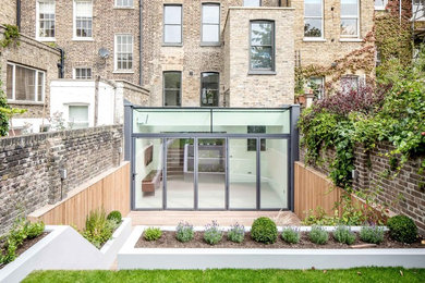 This is an example of a medium sized and gey contemporary glass terraced house in London with three floors, a flat roof and a green roof.