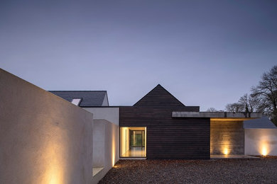Réalisation d'une grande façade de maison grise design en béton de plain-pied avec un toit à deux pans et un toit mixte.