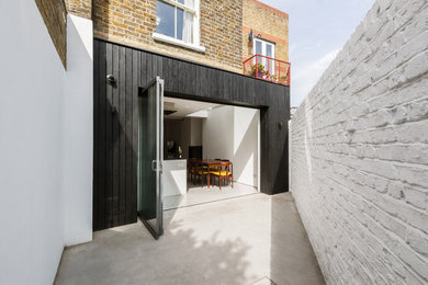 Small and brown contemporary two floor terraced house in London with wood cladding, a pitched roof and a tiled roof.