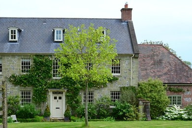 На фото: трехэтажный, зеленый дом в классическом стиле с облицовкой из камня и двускатной крышей
