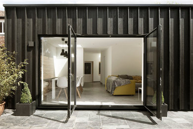 Cette photo montre une petite façade de maison noire tendance en bois de plain-pied avec un toit plat et un toit mixte.