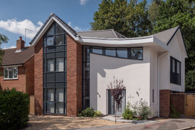 Imagen de fachada de casa moderna de tamaño medio de tres plantas con revestimientos combinados, tejado a dos aguas y tejado de teja de barro