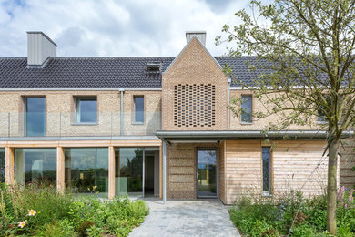 Diseño de fachada de casa beige campestre grande de dos plantas con tejado a dos aguas, tejado de teja de barro y revestimiento de piedra