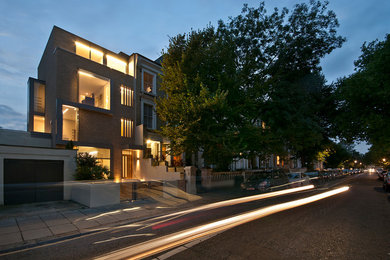 This is an example of a large and brown contemporary brick house exterior in London with three floors and a flat roof.