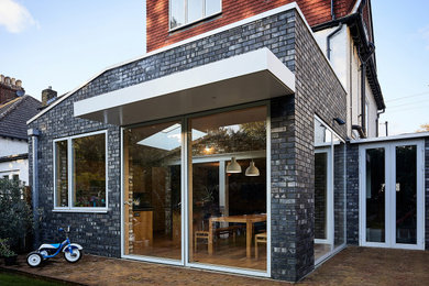 This is an example of a small and black contemporary bungalow brick semi-detached house in London with a flat roof and a mixed material roof.