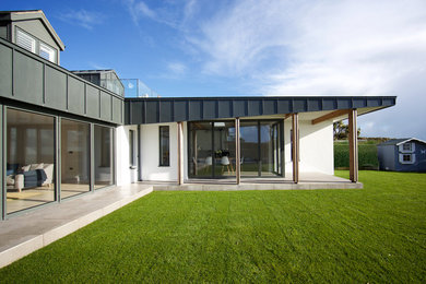 Aménagement d'une façade de maison métallique et grise contemporaine de taille moyenne et à un étage avec un toit mixte.