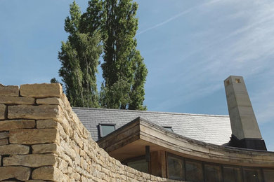 This is an example of a large contemporary two floor house exterior in Wiltshire with stone cladding, a pitched roof and a tiled roof.