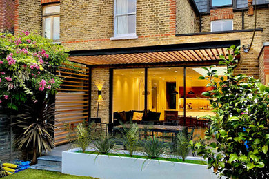 This is an example of a small contemporary brick and rear house exterior in London with three floors, a mansard roof and a tiled roof.