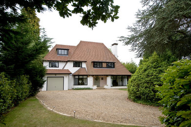 Example of a large arts and crafts white three-story stucco house exterior design in Surrey with a hip roof and a shingle roof