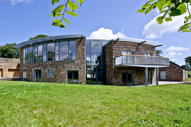 This is an example of a multi-coloured rural two floor detached house in Devon with stone cladding, a pitched roof and a metal roof.