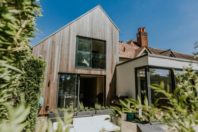 This is an example of a large and beige contemporary two floor semi-detached house in Surrey with wood cladding, a pitched roof and a mixed material roof.