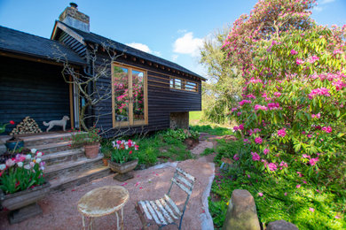 Photo of a small and black rustic two floor detached house in Devon with wood cladding, a pitched roof and a shingle roof.