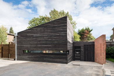 This is an example of a small and black contemporary bungalow detached house in London with wood cladding, a lean-to roof and a mixed material roof.