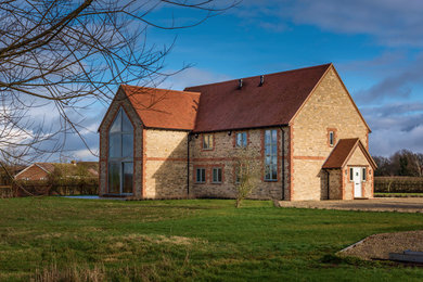 Réalisation d'une grande façade de maison multicolore tradition en pierre à un étage avec un toit à deux pans et un toit en tuile.