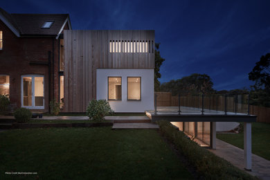 This is an example of a medium sized modern two floor detached house in Hampshire with wood cladding, a mixed material roof and board and batten cladding.
