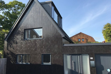 Ejemplo de fachada de casa negra nórdica de tamaño medio de tres plantas con revestimiento de madera, tejado a dos aguas y tejado de teja de barro