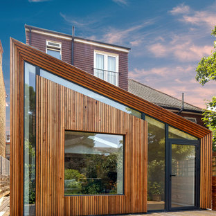 Large and brown contemporary one floor detached house in London with wood cladding and a lean-to roof.