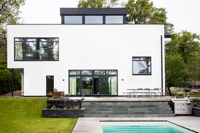 Aménagement d'une grande façade de maison blanche moderne en béton à un étage avec un toit plat.
