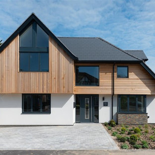 Large and white contemporary two floor detached house in London with wood cladding and a hip roof.