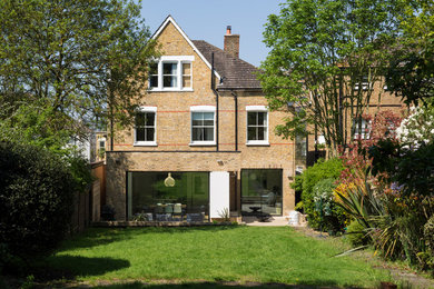 Photo of a yellow contemporary brick detached house in London with three floors and a mixed material roof.