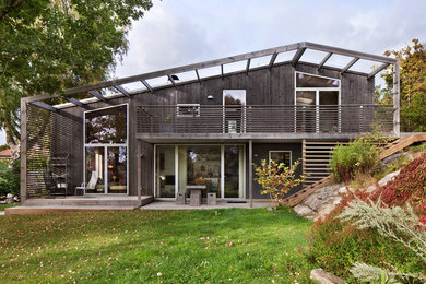 Imagen de fachada negra actual grande de dos plantas con revestimiento de madera y tejado a dos aguas