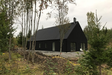 Foto på ett stort svart hus, med allt i ett plan, sadeltak och tak i mixade material