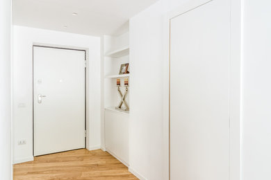 Ispirazione per un ingresso design di medie dimensioni con pareti bianche, parquet chiaro, una porta singola e una porta bianca