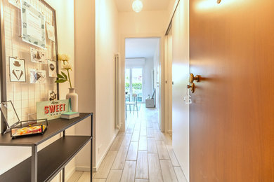 Immagine di un piccolo ingresso contemporaneo con pareti bianche, pavimento in gres porcellanato, una porta singola, una porta in legno chiaro e pavimento grigio