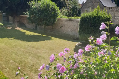 Diseño de jardín tradicional de tamaño medio en primavera en patio trasero con jardín francés, exposición total al sol y adoquines de piedra natural