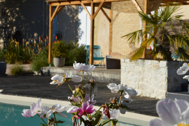 Cette image montre un jardin arrière rustique de taille moyenne et au printemps avec un massif de fleurs, une exposition ensoleillée et une terrasse en bois.