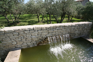 Ejemplo de jardín mediterráneo grande en patio trasero con fuente y exposición total al sol