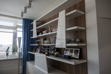 Foto de despacho actual pequeño con biblioteca, paredes blancas, suelo de madera en tonos medios, escritorio empotrado y suelo marrón