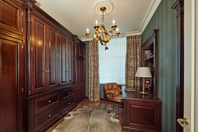 Imagen de despacho de tamaño medio con biblioteca, paredes verdes, suelo de madera en tonos medios y escritorio empotrado
