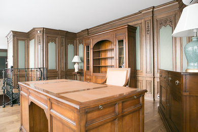 Пример оригинального дизайна: большое рабочее место в классическом стиле с коричневыми стенами, темным паркетным полом и отдельно стоящим рабочим столом без камина