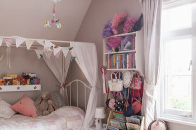 This is an example of a medium sized bohemian children’s room for girls in West Midlands with pink walls, medium hardwood flooring and brown floors.
