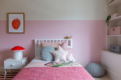 This is an example of a small contemporary children’s room for girls in London with beige walls, carpet and red floors.