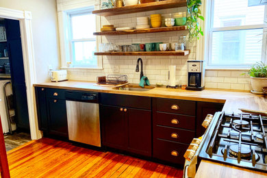 Enclosed kitchen - mid-sized industrial u-shaped dark wood floor and brown floor enclosed kitchen idea with a single-bowl sink, flat-panel cabinets, black cabinets, wood countertops, white backsplash, subway tile backsplash, stainless steel appliances, no island and brown countertops