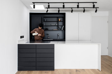 Imagen de cocina comedor contemporánea de tamaño medio con fregadero encastrado, armarios con paneles lisos, puertas de armario blancas, salpicadero negro, electrodomésticos negros y encimeras blancas