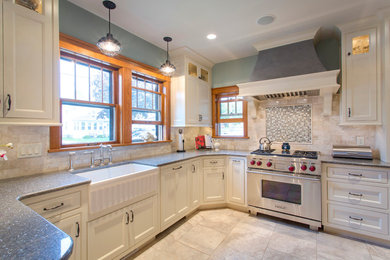 Klassisk inredning av ett kök, med en rustik diskho, släta luckor, vita skåp, bänkskiva i kvartsit, flerfärgad stänkskydd, stänkskydd i stenkakel, rostfria vitvaror, klinkergolv i porslin och en halv köksö