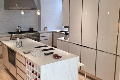 Example of a large transitional u-shaped marble floor eat-in kitchen design in New York with a single-bowl sink, flat-panel cabinets, white cabinets, marble countertops, white backsplash, stone slab backsplash, stainless steel appliances and an island