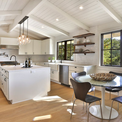 Inspiration for a mid-sized farmhouse u-shaped light wood floor and brown floor eat-in kitchen remodel in San Francisco with an island, a farmhouse sink, raised-panel cabinets, white cabinets, granite countertops, white backsplash, subway tile backsplash and stainless steel appliances