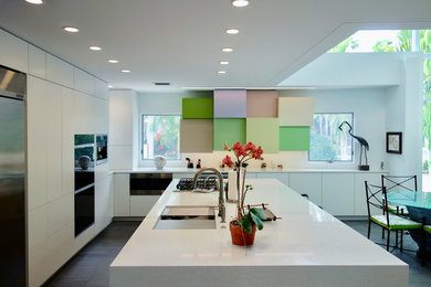 Photo of a large modern l-shaped kitchen/diner in Tampa with a submerged sink, flat-panel cabinets, white cabinets, engineered stone countertops, white splashback, stainless steel appliances, porcelain flooring, an island, grey floors and white worktops.