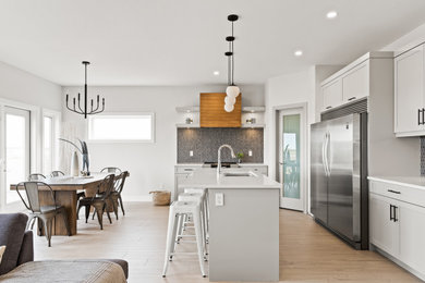 Example of a trendy l-shaped light wood floor eat-in kitchen design in Other with shaker cabinets, gray cabinets, quartzite countertops, gray backsplash, porcelain backsplash, stainless steel appliances, an island and white countertops