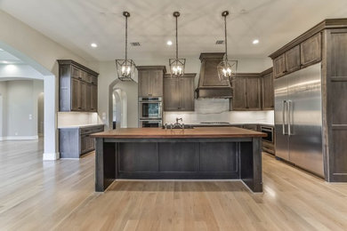 Photo of a large traditional grey and cream l-shaped kitchen/diner in Houston with a belfast sink, recessed-panel cabinets, medium wood cabinets, quartz worktops, stainless steel appliances, light hardwood flooring, an island, white splashback, stone slab splashback and brown floors.