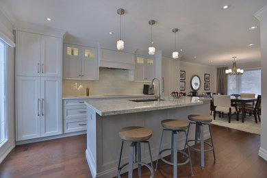 Mid-sized transitional single-wall light wood floor eat-in kitchen photo with an undermount sink, shaker cabinets, white cabinets, granite countertops, white backsplash, glass tile backsplash, stainless steel appliances and an island