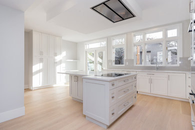 Große Klassische Küche in L-Form mit Schrankfronten im Shaker-Stil, weißen Schränken, Küchenrückwand in Grau, Küchengeräten aus Edelstahl, hellem Holzboden und Kücheninsel in Vancouver