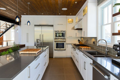 Photo of a large contemporary l-shaped kitchen/diner in Montreal with a double-bowl sink, shaker cabinets, white cabinets, engineered stone countertops, grey splashback, glass tiled splashback, stainless steel appliances, ceramic flooring and an island.