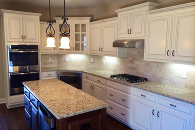 Example of a mid-sized classic u-shaped medium tone wood floor eat-in kitchen design in Other with an undermount sink, raised-panel cabinets, white cabinets, granite countertops, beige backsplash, ceramic backsplash, stainless steel appliances and an island